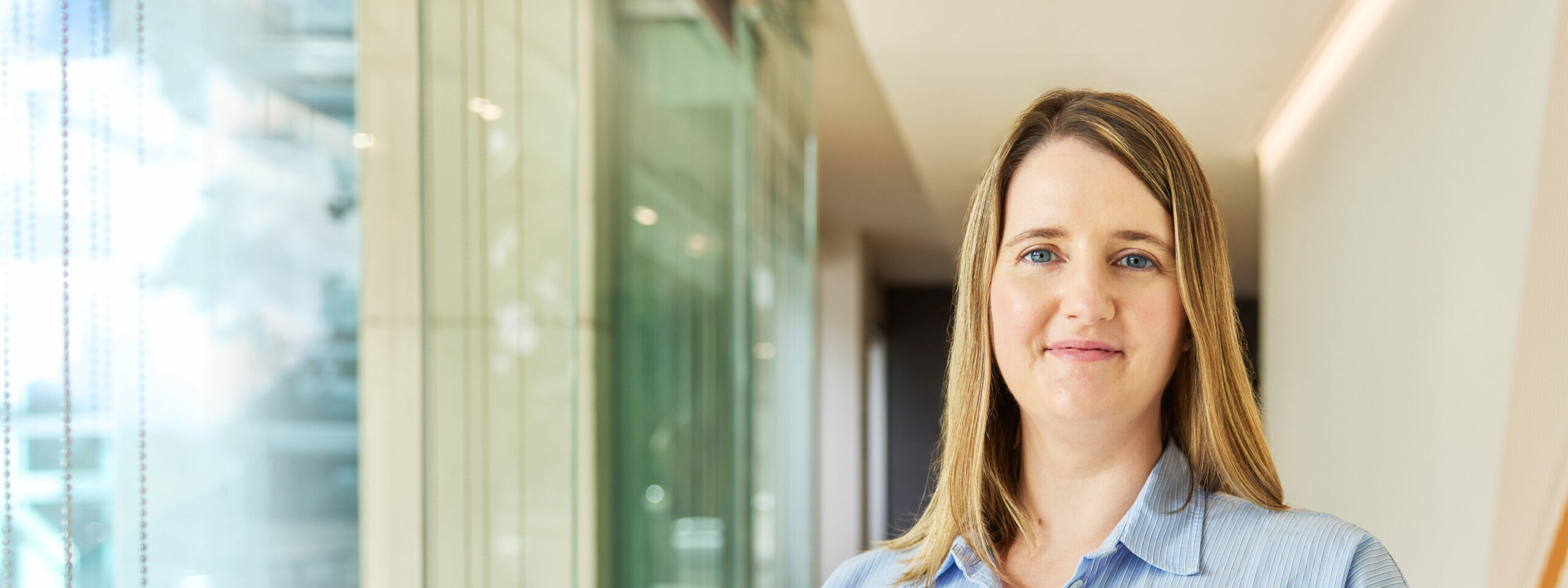 Dr Danielle Coupland standing in a light filled hallway lined with glass windows