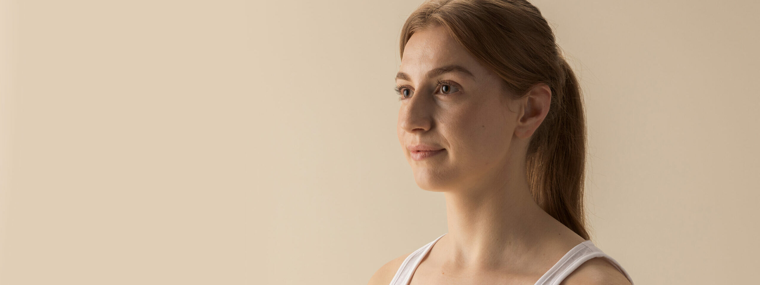 Female Workplace Injury, RTW & MVA patient in white tank top standing against a neutral background